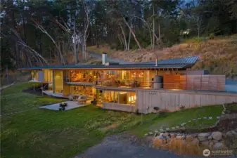 At dusk, the residence glows warmly against the landscape, highlighting the nearly 10,000± sq ft architectural design and seamless indoor-outdoor connection overlooking San Juan Island’s pristine west side shoreline.