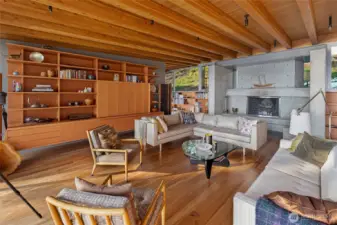 The sophisticated great room showcases exposed timber beams, custom built-ins, and a sculptural concrete fireplace, creating a warm yet modern gathering space designed to frame the surrounding San Juan Island natural landscape.
