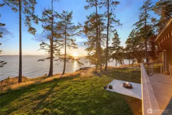 Golden sunset light pours across the property, illuminating the lawn and patio while the horizon stretches across Haro Strait toward the Olympic Mountains—a signature experience of San Juan Island west side living.