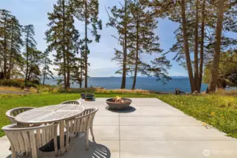 Entertain or unwind on the expansive waterfront patio featuring a firepit and outdoor dining space, perfectly positioned to take in sweeping views across the water and surrounding islands.