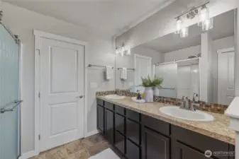 Dual vanity in the primary bathroom with a linen closet and walk in shower.