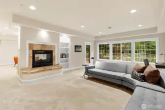 Light-filled living room featuring a wall of windows overlooking the forest, custom built-ins, and a gas fireplace, with direct access to the covered patio for seamless indoor-outdoor living.