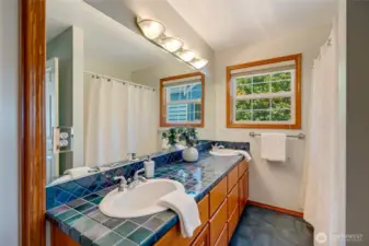 Upstairs full bath with double vanity, tiled counters, and tub/shower combo, accessible from both the bedroom and hallway.