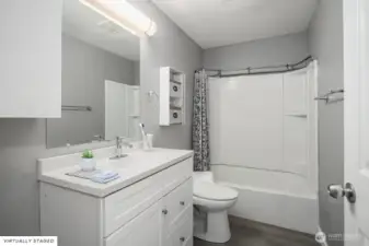 Clean and updated bathroom with modern vanity, large mirror, and a combination tub/shower with built-in shelving.