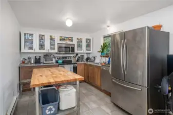 Unit 1 Updated kitchen with stainless steel appliances, tile flooring, and mixed wood + white cabinetry with glass-front uppers for modern storage and display.