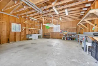 Interior of 2 car garage, with storage shelving, benches and 2 large windows.