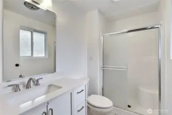 Fresh and modern primary bathroom featuring a sleek white vanity with quartz countertop, brushed nickel fixtures, and an oversized mirror for a bright, polished feel. The step-in shower with sliding glass doors offers ease and functionality, completing this well-appointed private space.
