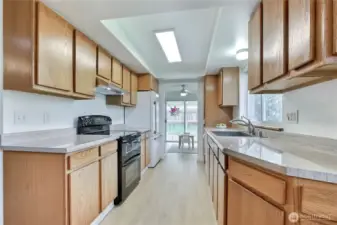 Bright and functional galley-style kitchen with ample cabinet storage, solid-surface countertops, and all appliances included—featuring a brand new refrigerator, hood, and deep stainless steel sink! Thoughtful layout offers excellent prep space and a clean, modern look with updated flooring and a pass-through view to the bonus room and backyard. Natural light streams in from the window and slider, enhancing the warm, inviting feel.