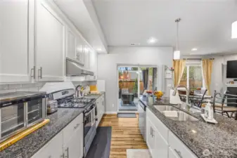 bright open kitchen with white shaker cabinets, granite countertops, subway tile backsplash, and stainless steel appliances.