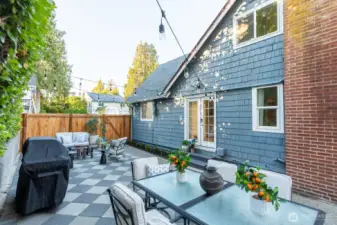 Stylish checkered paver patio with privacy fencing and string lights. Wonderful spot for entertaining or relaxing outdoors.