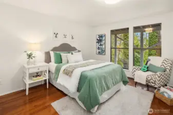 Bright lower-level bedroom featuring hardwood floors and large windows framing tranquil greenery