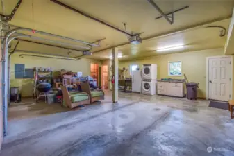 The oversized garage contains two mechanical rooms, a built-in workbench (on left, covered with personal belongings), a sink, freezer, laundry center and cabinetry. Door leads to stairs to the deck