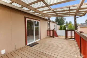 Second view of covered trex deck with wood wrailings leading to sliding glass doors and back yard fund