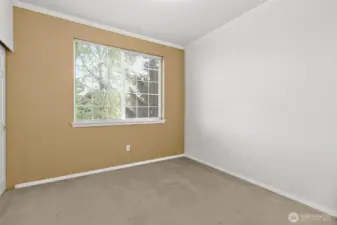 This inviting second bedroom offers a large window that fills the space with natural light and provides a peaceful view of the surrounding greenery. Neutral tones and clean lines create a comfortable and flexible space—perfect for a guest room or nursery.