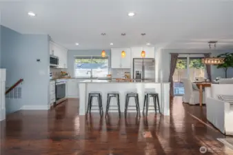 The immaculate, updated kitchen showcases quartz counters, white cabinets, designer lighting, newer stainless steel appliances, and gorgeous engineered hardwood floors.