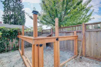 Fenced dog run by front gate and raised beds on south side of home.