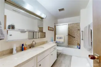 Bathroom with granite counters, laminate flooring, and tub/shower with tiled surround.
