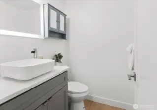 Fully renovated half bath, featuring new grey shaker vanity, luxury vinyl plank flooring, new toilet & Lux Hardwired LED Mirrors.