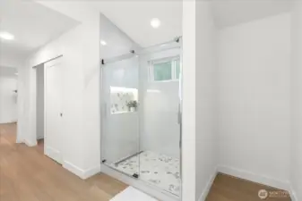 Primary shower upgraded with tile, linear drain, niche shelf with LED lighting, and frameless glass doors. Luxury vinyl plank flooring and craftsman style square baseboards. Extra space to the right perfect for shelving for linens.