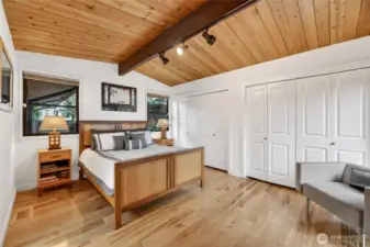 Primary bedroom with wall of closets under vaulted cedar.