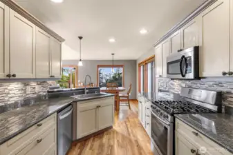 The kitchen dazzles with granite countertops, stainless steel appliances, gas range, and a mosaic tile backsplash. An open bar area makes entertaining effortless while soaking in views toward the deck and dining area.