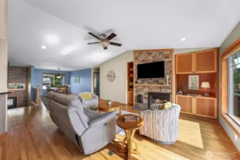 A second angle of the living room highlights the integration of comfort and craftsmanship, featuring built-in shelving, a stone hearth, and plush seating—perfect for evenings by the fire. The layout blends naturally into the dining space beyond.