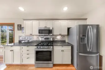 This straight-on view showcases the stainless steel appliance suite—including a gas range and microwave—accented by soft-close cabinetry and sleek mosaic tile for a contemporary, polished look.