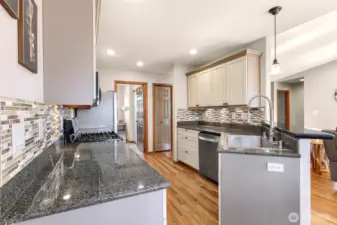 A spacious galley layout and warm hardwood floors create ease of movement in this updated kitchen, featuring ample prep space, stylish backsplash, and open sightlines to the dining and living areas.