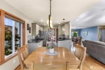 Open-concept dining and kitchen area featuring granite countertops, stainless steel appliances, and a chic tile backsplash. Light cabinetry complements the rich wood floors, with ample natural light streaming through the large windows