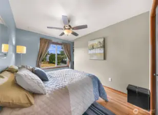 The guest bedroom offers a peaceful escape with soft blue walls, hardwood floors, and a large picture window overlooking the landscaped yard—ideal for visitors or a flexible office space.