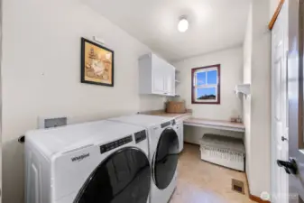 The bright laundry room includes front-loading Whirlpool washer/dryer, extra counter space, a window for light, and built-in seating—designed for comfort and efficiency.