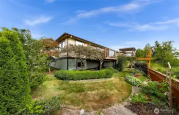 The backyard is a lush, terraced oasis with manicured landscaping, mature trees, and flowering shrubs—creating a private escape in the heart of the gated Sealinks community.