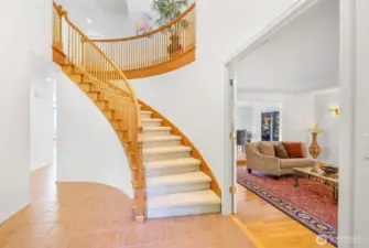 Inside, the sweeping curved staircase serves as a striking centerpiece of the foyer. The open design, tile flooring, and soaring ceiling create a bright and inviting introduction to the living spaces beyond.