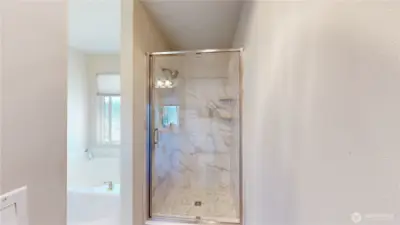 Tiled walk-in shower in the primary suite, featuring a glass enclosure, modern fixtures, and built-in shelving.