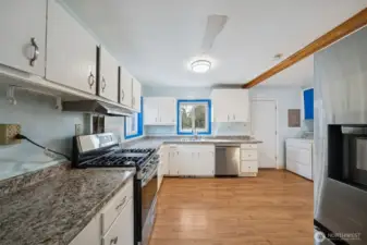Kitchen with new counters, barely used gas range/stove, new dishwasher, and new flooring. Door by the dryer leads to the Trex deck outside.