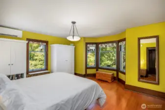 Bright primary suite with windows on two sides and warm wood floors.