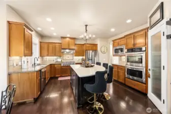 Gourmet kitchen features a large center  island, sleek tile backsplash, and high-end  stainless steel appliances with Kenmore Elite  gas cooktop & new 2023  microwave—including a double oven and  built-in beverage refrigerator.