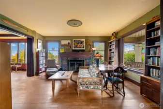 Oversized living room featuring a classic fireplace, large picture windows with natural light, built-in bookshelves, and gleaming hardwood floors.