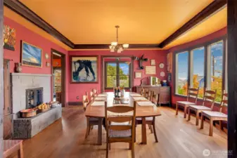 Dining room with seating for a large gathering, flanked by a fireplace and oversized windows with views of the neighborhood.