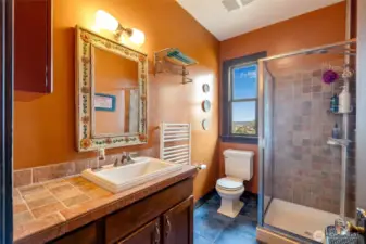 Primary en-suite bath with tile work, decorative vanity, glass-enclosed shower, and a window with natural light.