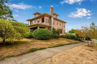 Stunning side and front exterior view of this grand historic home, showcasing its timeless architecture, stone chimney, large front porch, and beautiful corner lot setting.