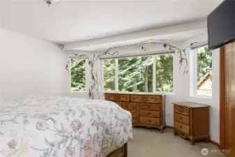 Primary suite on main level with 2 closets, view to backyard trees and playhouse, large windows with hand-painted wall art by Langley artist, Darla Neilson