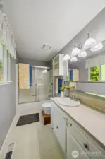 The full primary bath includes a glass sliding shower door, extra cabinet storage and sliding mirrored toiletry shelf below the vanity mirror.