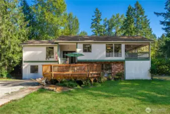 Inviting split-level exterior framed by mature trees, with a spacious front deck perfect for outdoor seating and curb appeal that blends brick and wood siding.