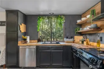 Updated kitchen with wood countertops, sleek black cabinetry, and a window over the sink framing peaceful outdoor views.