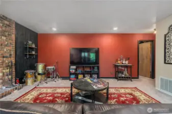 This vibrant recreation room offers plenty of space for entertainment and relaxation, featuring a bold red accent wall, built-in shelving, and a designated area for games and music. The layout is perfect for hosting movie nights, jam sessions, or casual gatherings with friends and family.