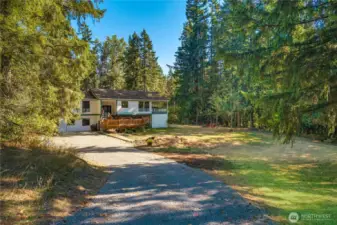 Charming home set against a backdrop of towering evergreens, with an open front yard and inviting deck space for relaxing outdoors.