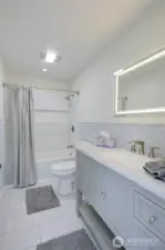 Main floor guest bathroom featuring updated finishes, LED backlit mirror, shower/tub combo, with clean lines and a fresh, modern feel