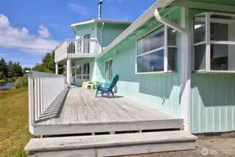 The expansive back deck is the ultimate outdoor retreat, offering plenty of space to relax and entertain with peek-a-boo canal views, and a second-story balcony above — all wrapped in the charming coastal character of this cheerful seafoam-colored home.