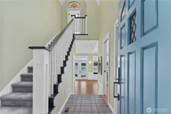 Inviting entry with soaring ceilings, classic staircase, and sightlines leading to stunning waterfront views beyond.